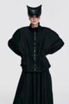 Model wearing a black drawstring waist jacket with raglan sleeves and zip front by KimC Studio.