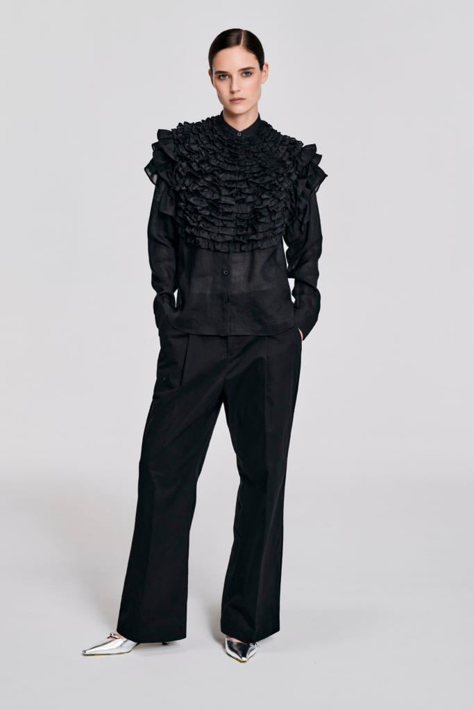 Model wearing a black hemp ruffle sleeve shirt with sculptural shoulder ruffles, pointed collar, button-front closure, and relaxed silhouette by KimC Studio.