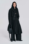 Model wearing a black hooded cotton coat with oversized longline silhouette, drawstring hood, wide sleeves, cuff tabs, and back strap detailing by KimC Studio.