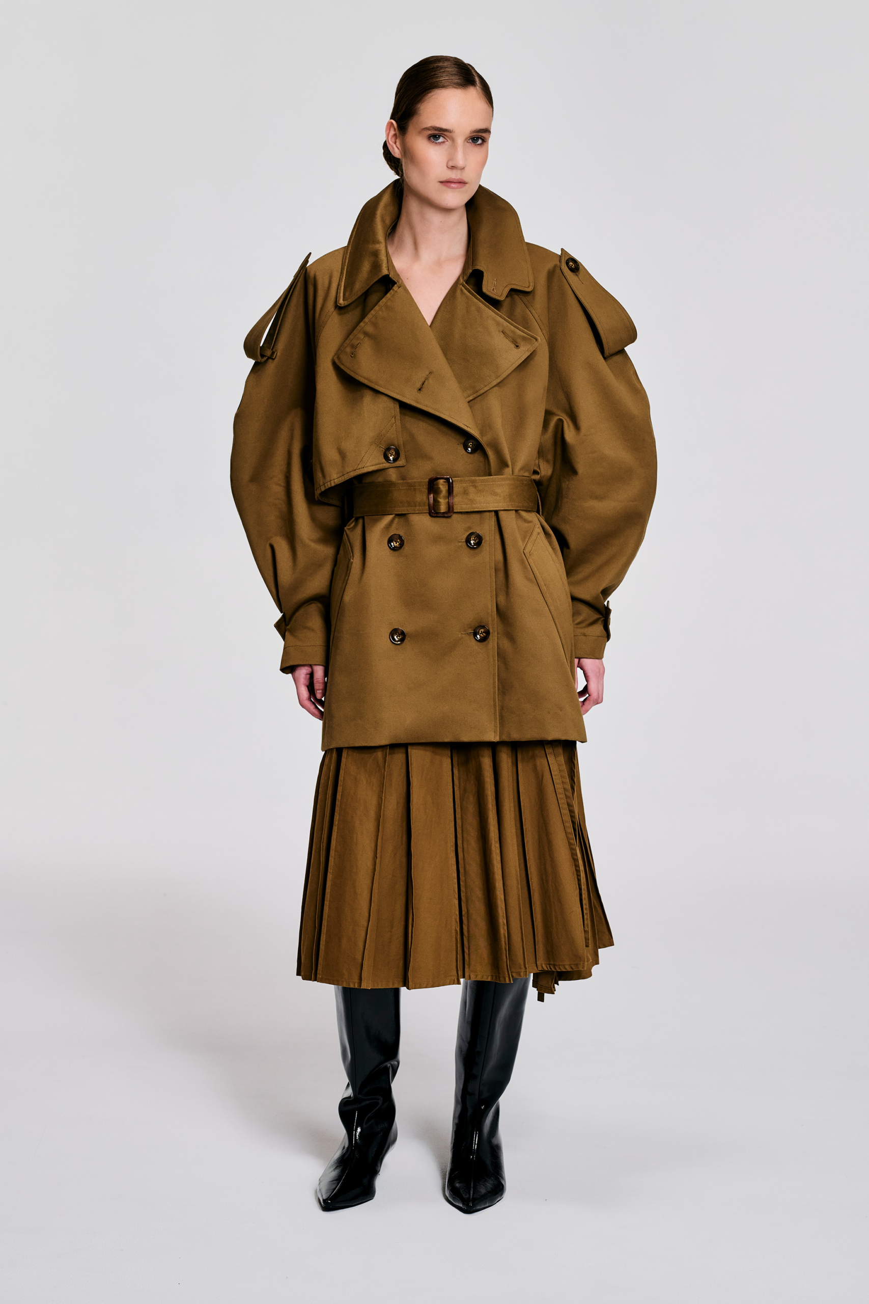 Model wearing camel cropped cotton trench jacket with matching pleated skirt and black boots by KimC Studio