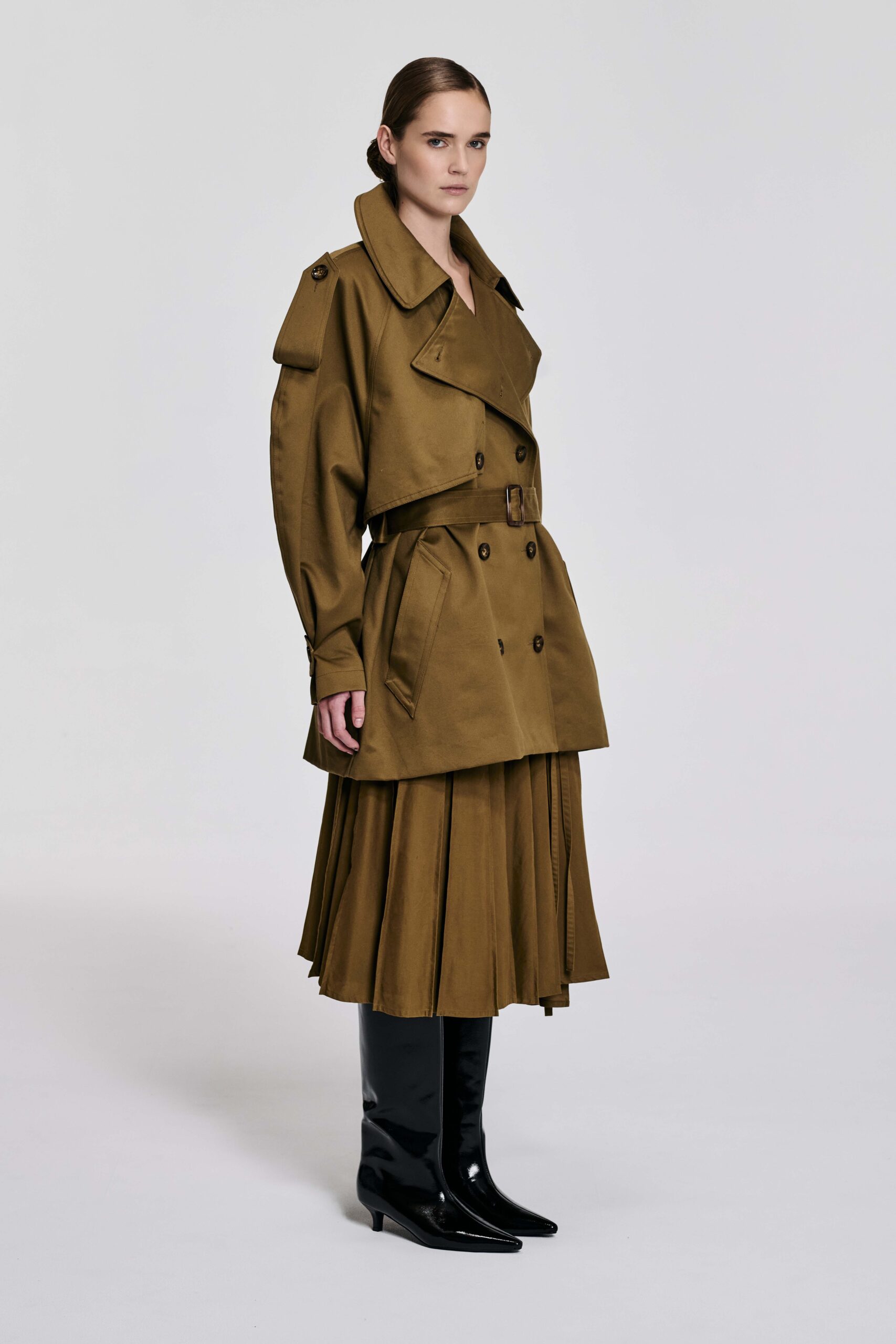 Model wearing camel cropped cotton trench jacket with matching pleated skirt and black boots by KimC Studio