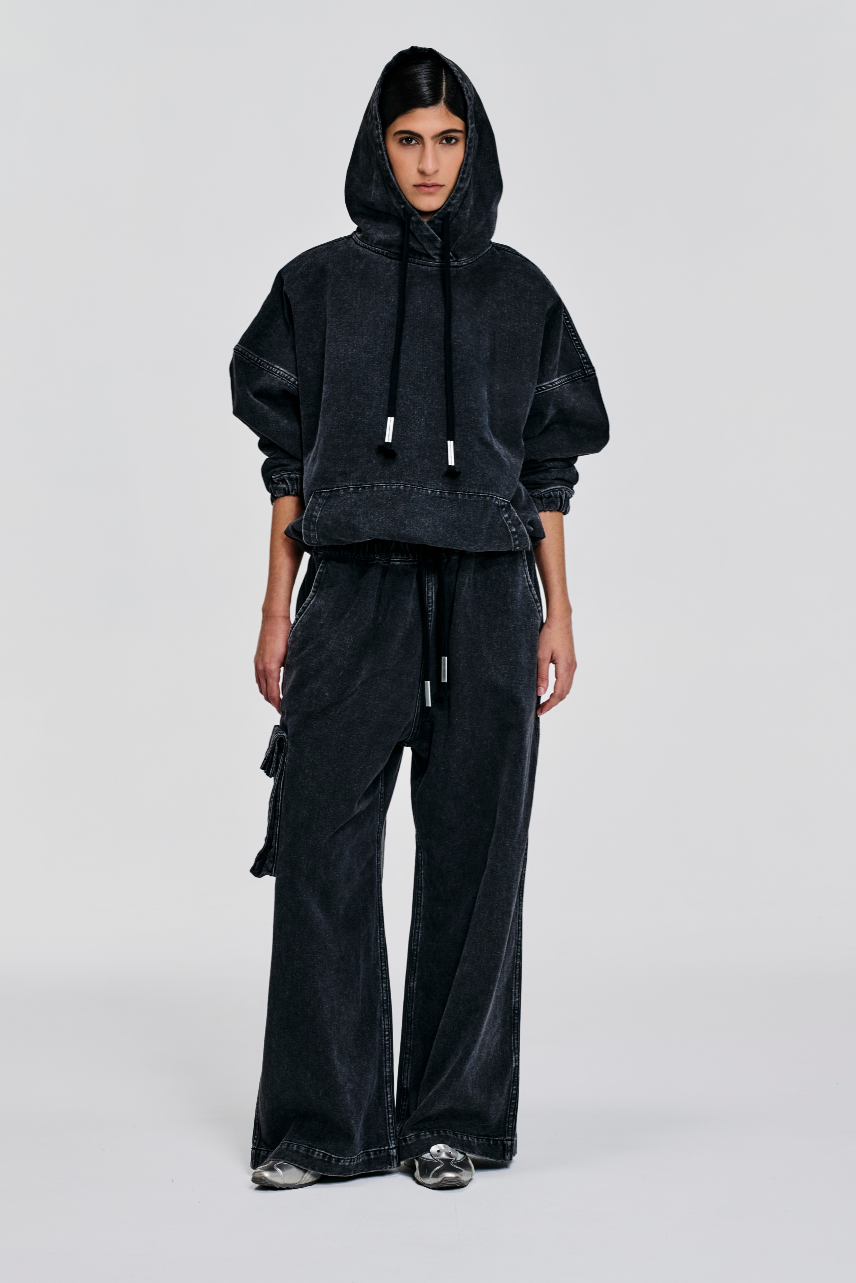 Front-view-of-model-wearing Enzyme-washed black denim hoodie with oversized fit, dropped shoulders, cropped hem, hood ties, and contrast stitching by KimC Studio.