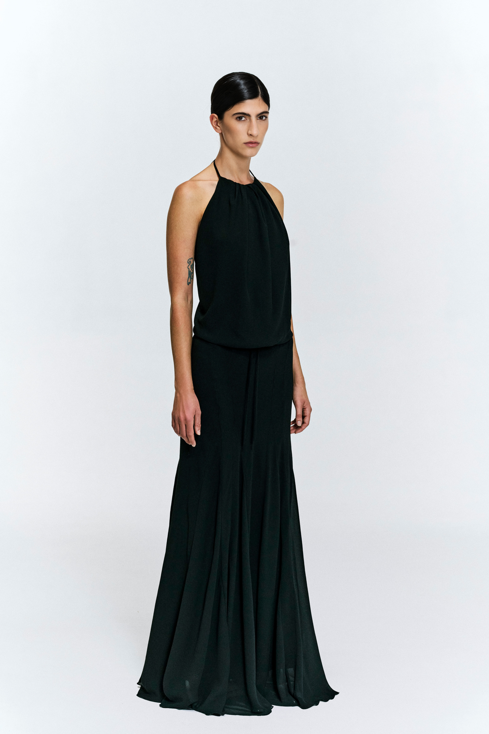 Model wearing a gathered halter maxi dress with relaxed blouson bodice, adjustable waist tie, satin lining and bias-cut floor-length skirt by KimC Studio.