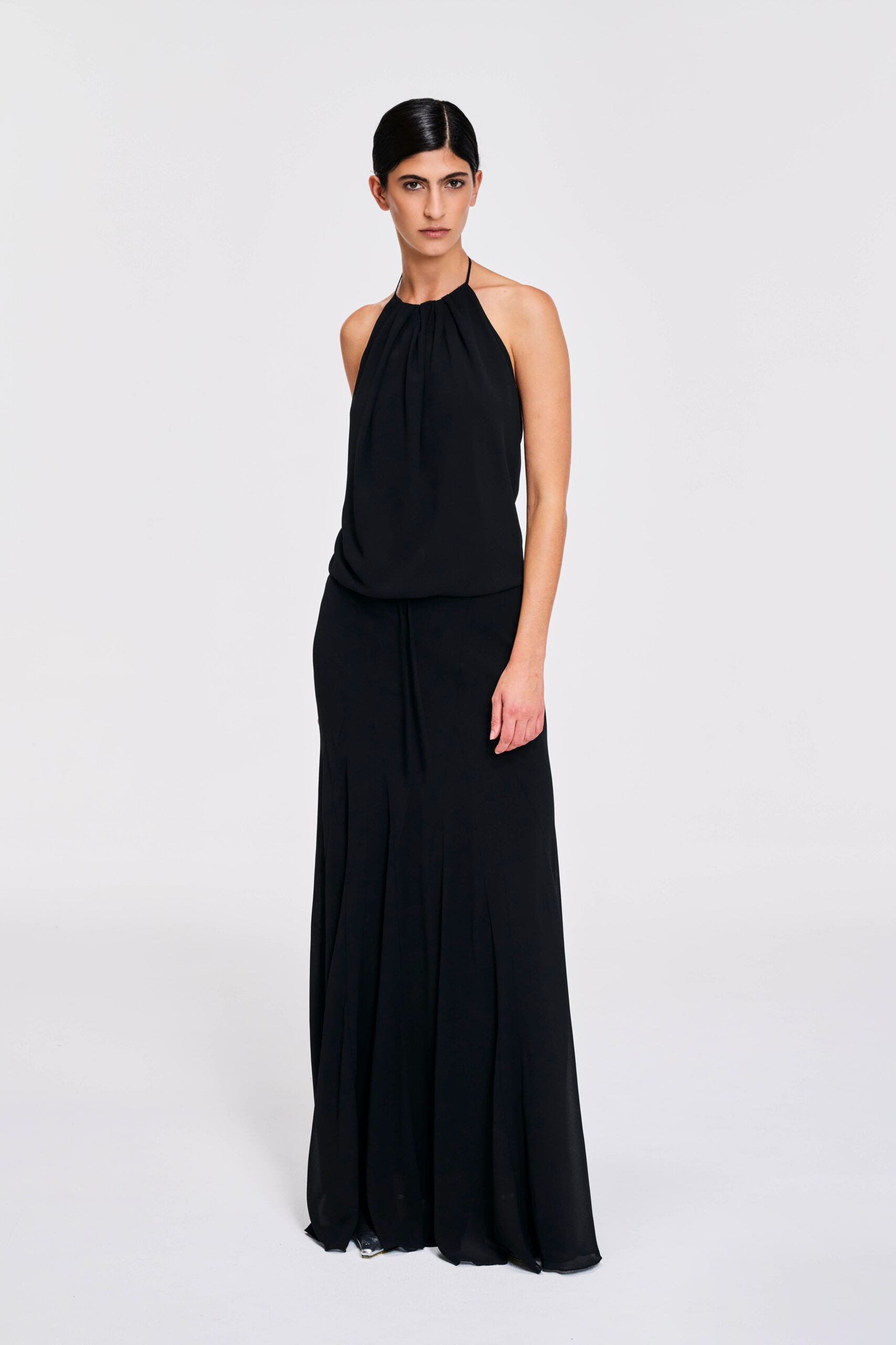 Model wearing a gathered halter maxi dress with relaxed blouson bodice, adjustable waist tie, satin lining and bias-cut floor-length skirt by KimC Studio.