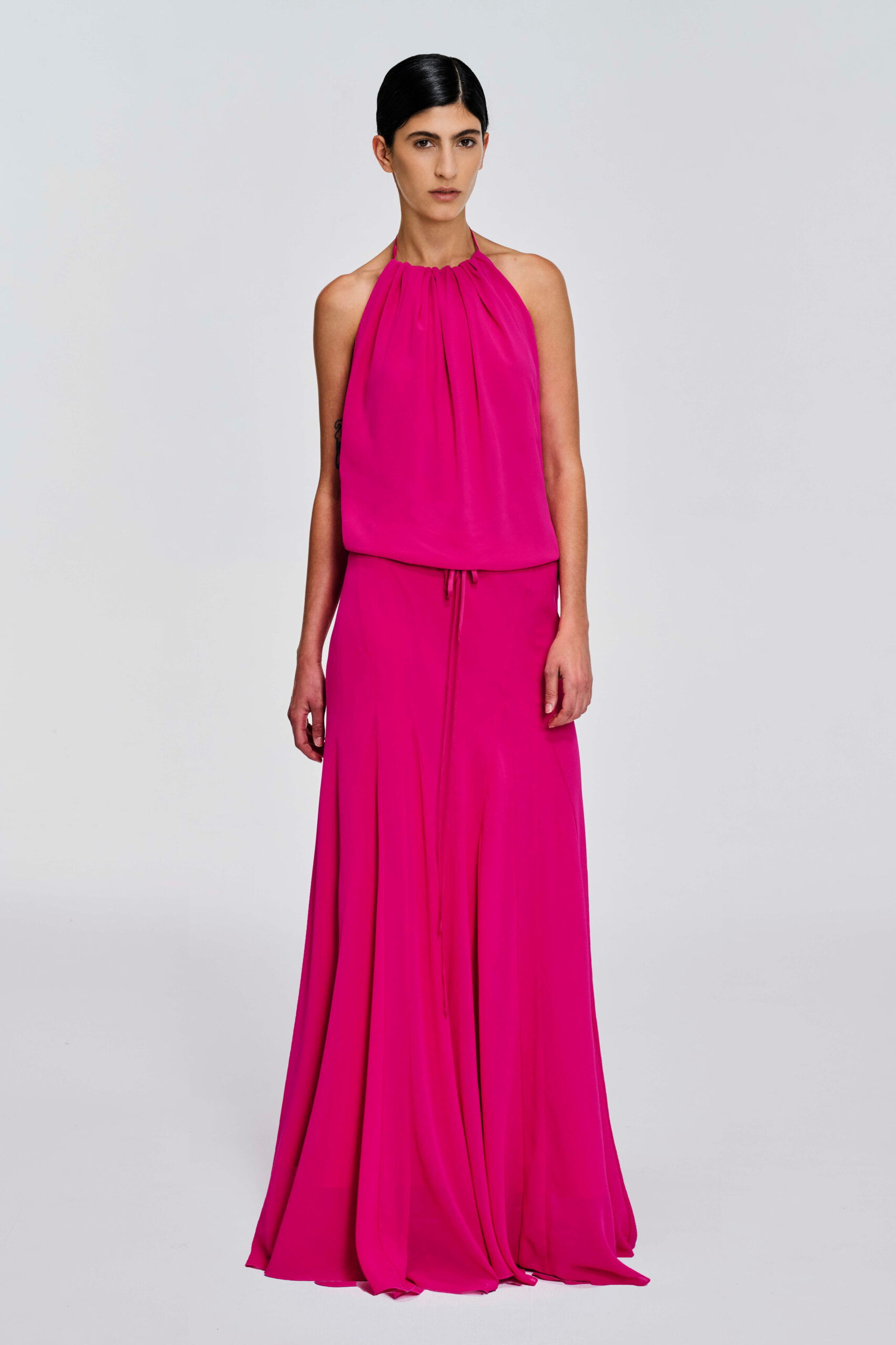Model wearing a gathered halter maxi dress with relaxed blouson bodice, adjustable waist tie, satin lining and bias-cut floor-length skirt by KimC Studio.