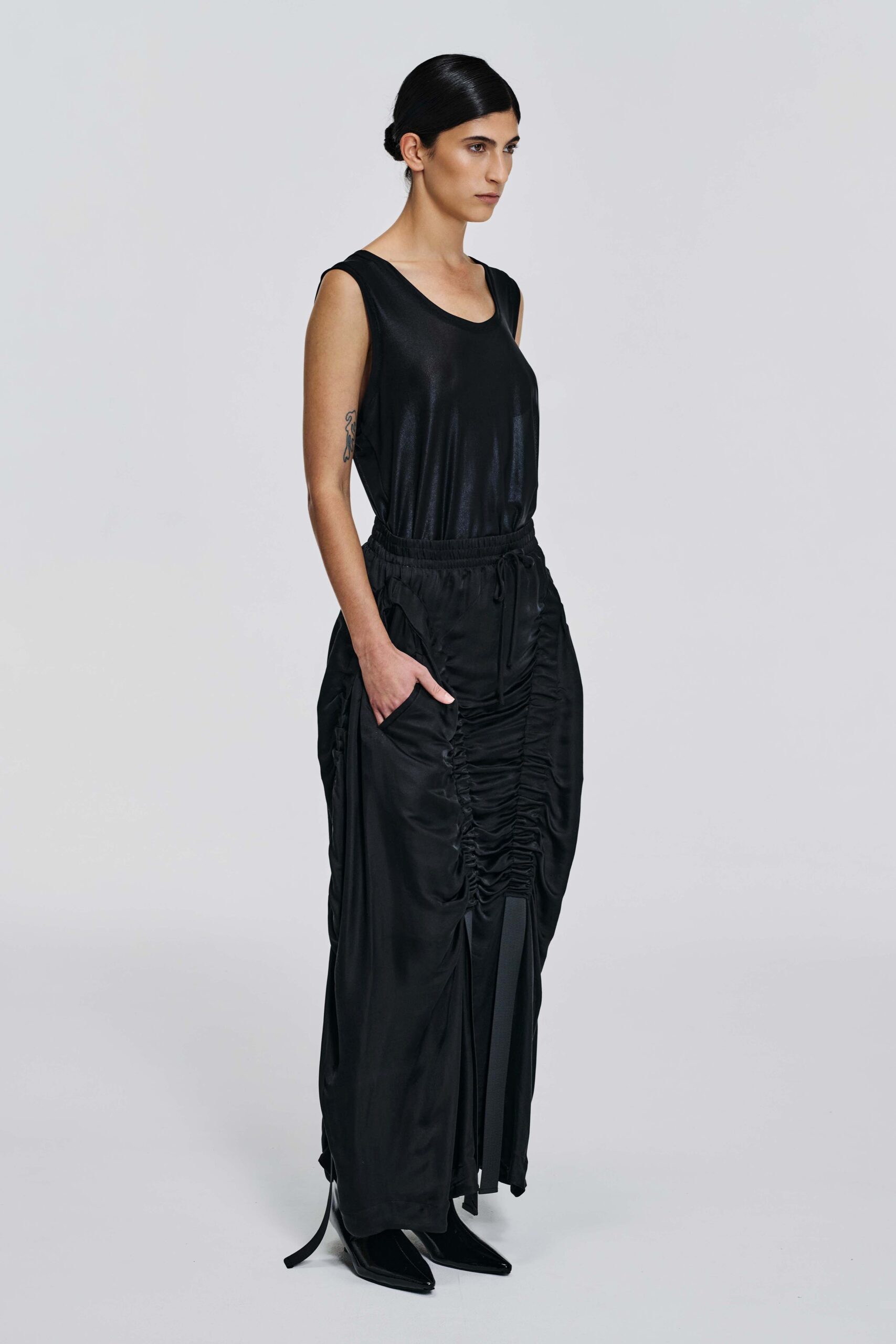 side view of Model wearing a black silk parachute skirt with ruched centre-front detailing, side pockets, and elongated ties by KimC Studio.