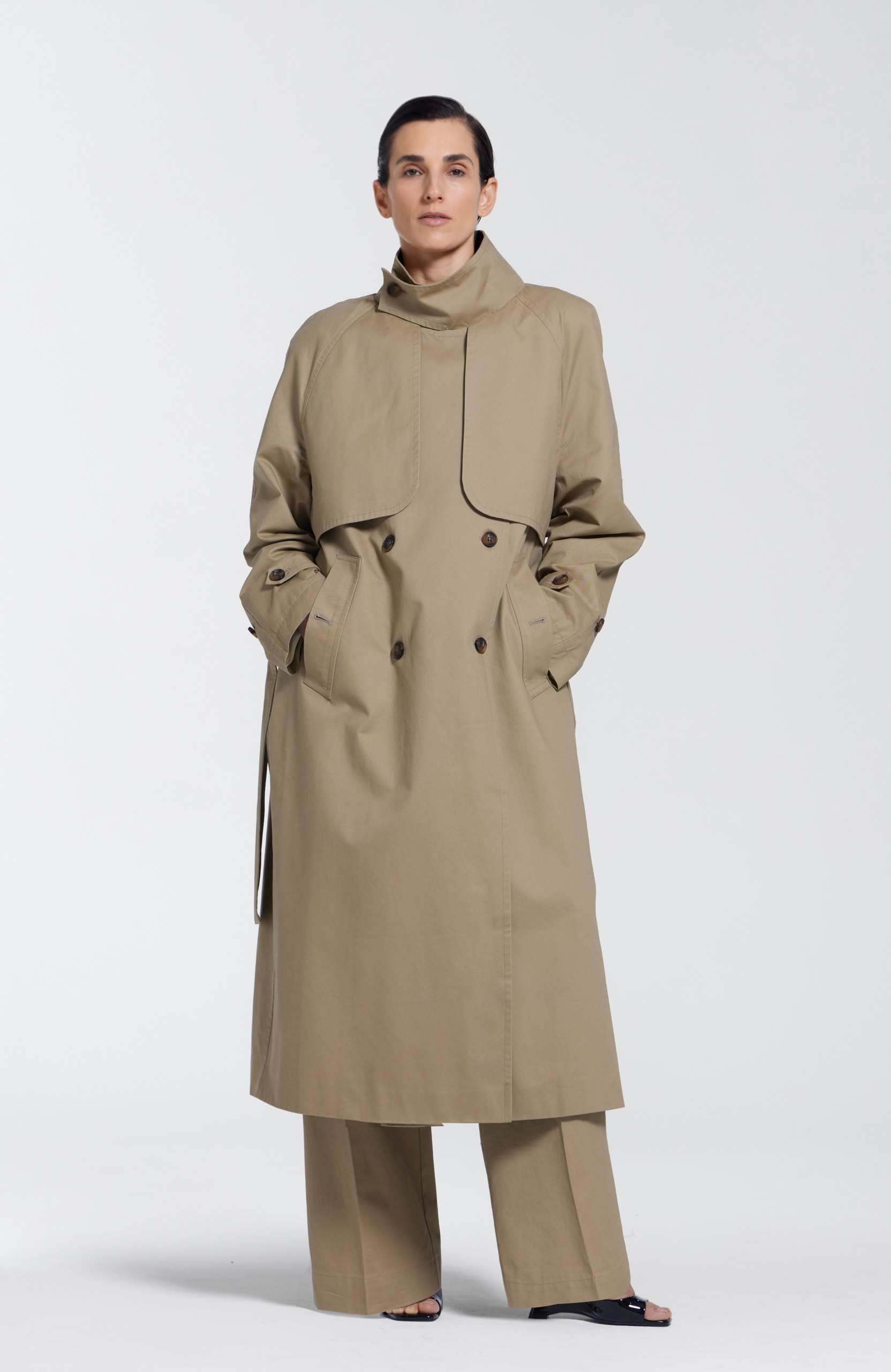 Model wearing a beige khaki 100% cotton trench coat with standing collar, waist tie, and silk lining by KimC Studio.