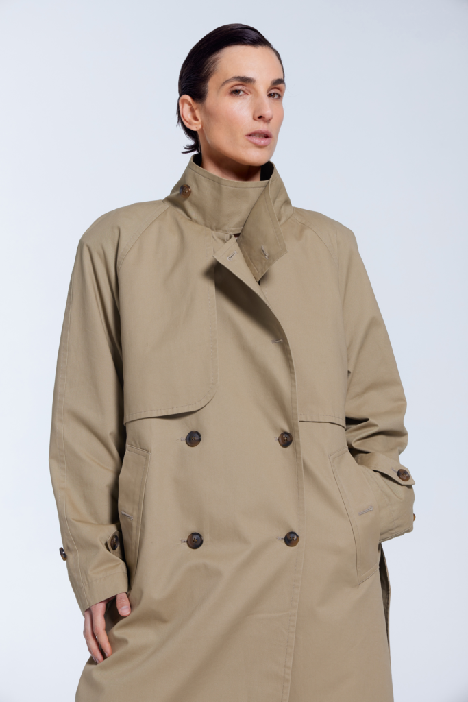 Model wearing a beige khaki 100% cotton trench coat with standing collar, waist tie, and silk lining by KimC Studio.