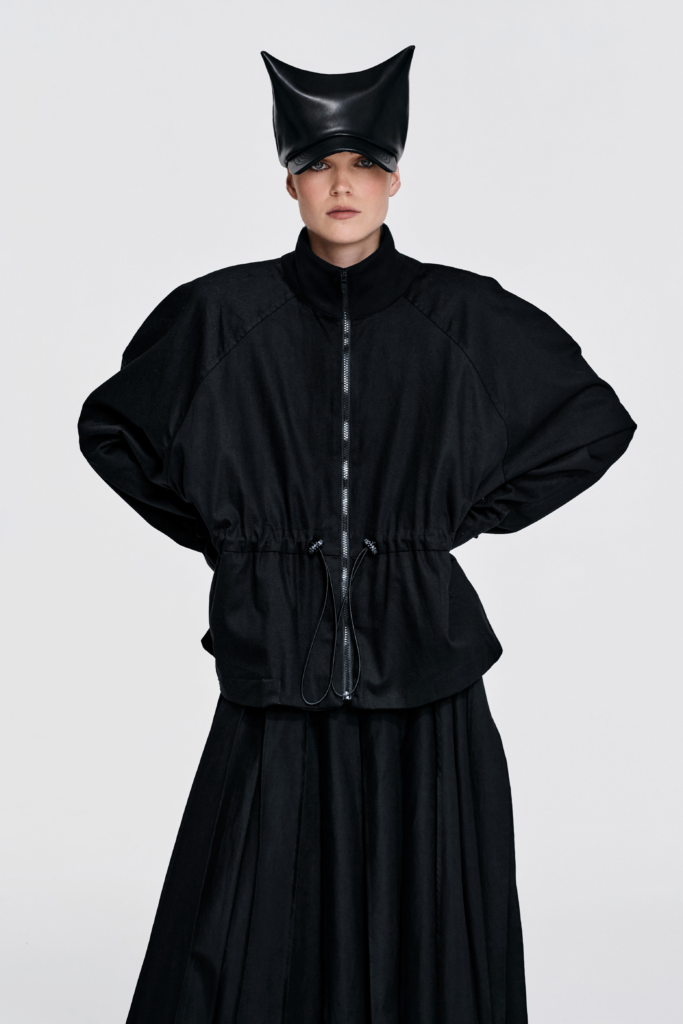 Detail view of black cotton jacket with curved layered panel and gathered lower section